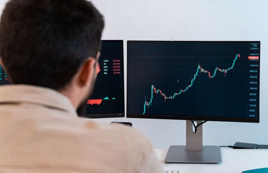 Young caucasian male finance broker analyzing stock graphs while trading from modern home office. Trader working with computer. High quality photo