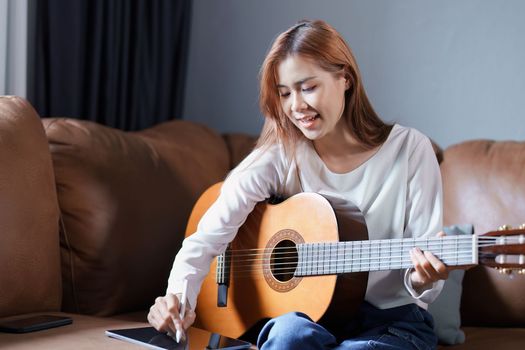 Portrait of young asian woman playing guitar on sofa relaxing stress on vacation.