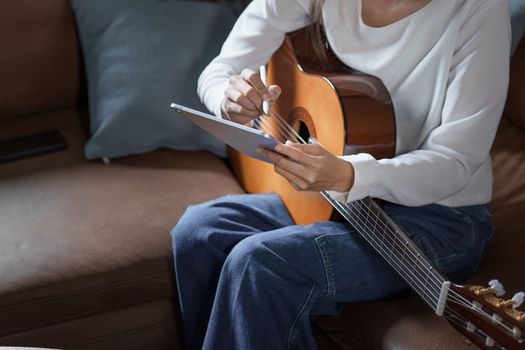 Portrait of young asian woman playing guitar on sofa relaxing stress on vacation.