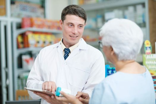 Smart male pharmacist at the drugstore wearing white gown talking, giving advice, explaining, suggesting, and recommending to client or patient about the prescription and medications. Medicine and healthcare concept.