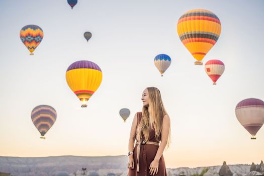 Tourist woman looking at hot air balloons in Cappadocia, Turkey. Happy Travel in Turkey concept. Woman on a mountain top enjoying wonderful view.