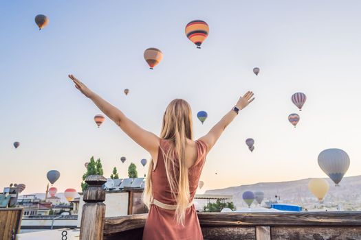 Tourist woman looking at hot air balloons in Cappadocia, Turkey. Happy Travel in Turkey concept. Woman on a mountain top enjoying wonderful view.