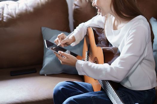 Portrait of young asian woman playing guitar on sofa relaxing stress on vacation.