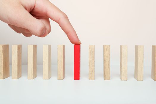 Domino stands and his finger points to the red one among all the wooden ones. Index finger on the domino