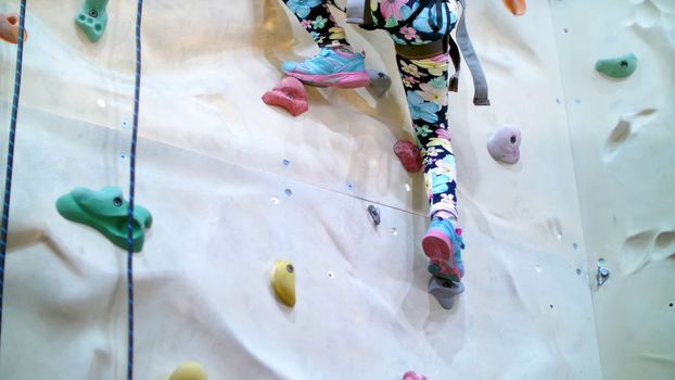 child climbs on a special wall for mountaineering. the girl of seven years in safety equipment is engaged in rock climbing on a special training vertical wall,. High quality photo