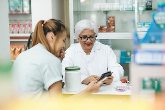 Female senior pharmacist at the drugstore wearing white gown talking, giving advice, explaining, suggesting, and recommending to client or patient about the prescription and medications. Medicine and healthcare concept.