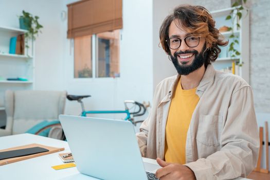 Successful hispanic male freelancer at the workplace, looks directly at the camera, smiling. Joyful handsome guy at webinar training or online conference. High quality photo