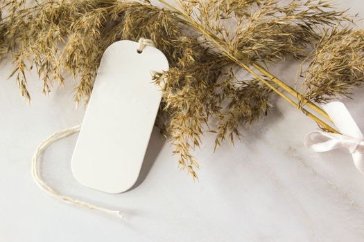 White tag mockup on a white background with silk ribbon and dry plants, element for packing. Label product mockup copy space for text and natural eco design