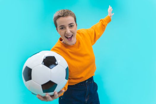 Screaming young woman girl football fan in orange sweater isolated on blue background. Sport leisure lifestyle concept. Cheer up support favorite team with soccer ball. High quality photo