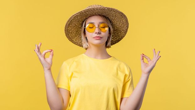 Calm woman relaxing, meditating, refuses stress. Sunny girl breathes deeply, calms down yellow studio background. Yoga, moral balance, zen concept. High quality photo