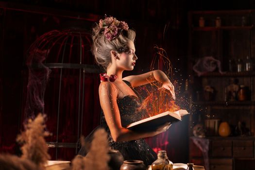 Charming woman witch flowers in hair vintage black dress with book of spell in the old castle. Halloween. Celebration. Witchcraft concept, fairy tale mystic atmosphere. Conjure magic spells