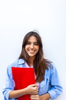 Vertical portrait of happy, smiling female university student looking at camera holding red folder. Education concept.