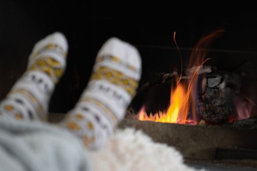 Girl resting and warming her feet by a burning fireplace in a country house on a winter evening. Selective focus.