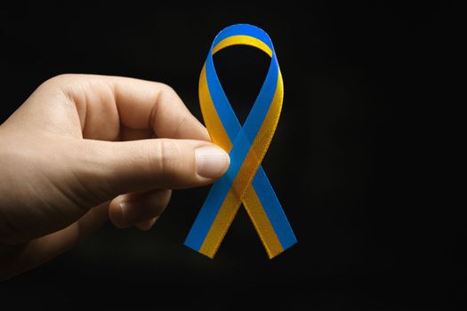 blue and yellow ribbon in female hands on dark background. concept needs help and support, truth will win