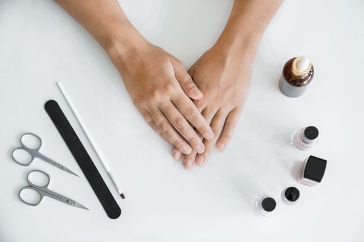 Concept of hand care. Women's hands without manicure are lying on table before starting manicure. Hands in close-up, manicure accessories are lying next to her on table. Top view, without a face.