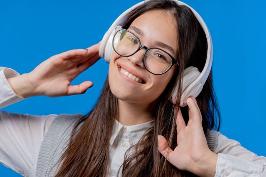 Happy student teenager listening music, enjoying dance with headphones on blue studio backdrop. Radio, wireless modern sound technology, online player. High quality photo