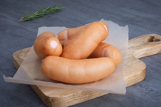 Several sausages lie on parchment paper on a wooden cutting board. Selective focus.