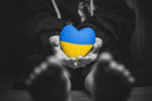 child hold painted yellow and blue heart in small hands. black and white color. concept needs help and support, truth will win