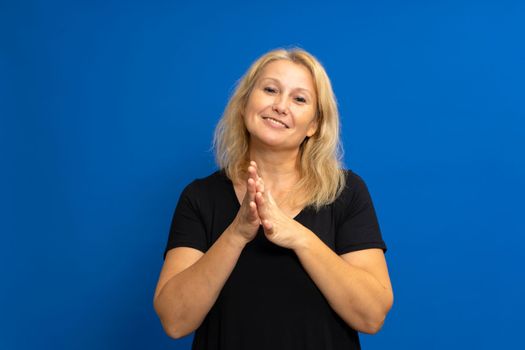 Pretty blonde caucasian woman feeling happy and successful, smiling and applauding, saying congratulations with a clap against blue colored wall