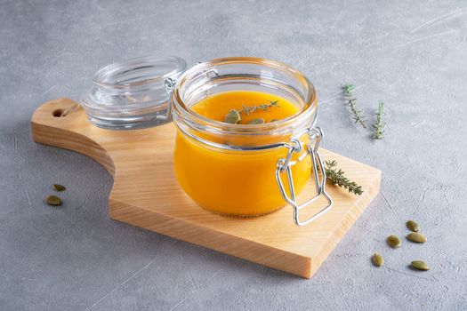 Pumpkin puree soup with pumpkin seeds and thyme in a glass jar on a wooden kitchen board. The concept of healthy nutrition from seasonal vegetables. Selective focus.