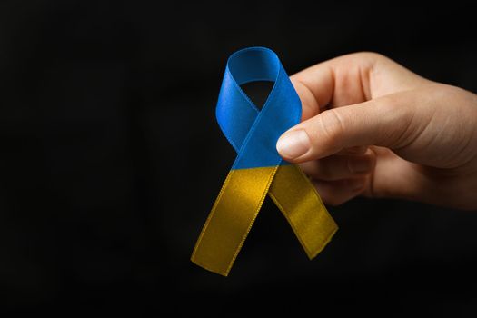 blue and yellow ribbon in female hands on dark background. concept needs help and support, truth will win