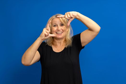 Caucasian happy blonde woman making frame with fingers isolated on a blue background.
