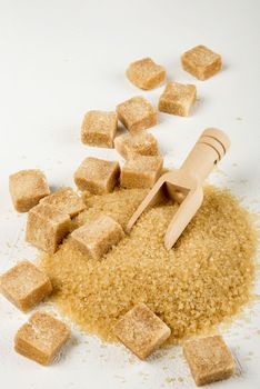 Brown cane sugar is also sprinkled in lumps on a light surface. Wooden scoop for bulk products. Selective focus. Vertical orientation, space for text.