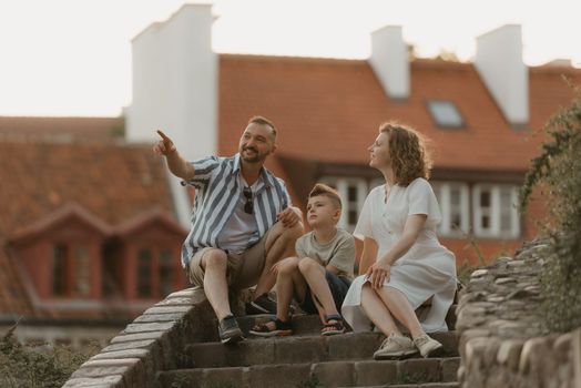 A family is discussing on the stairs between roofs in an old European town. A happy father, mother, and son are having fun in the evening.