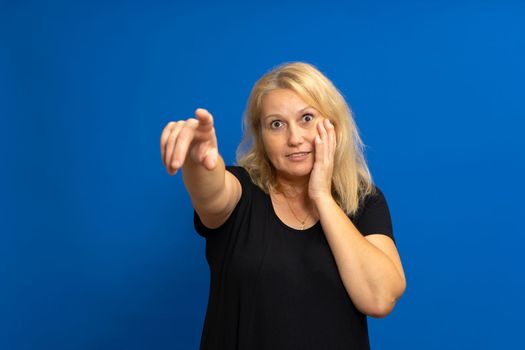 Surprised attractive cute blonde straight-haired caucasian woman in casual black t-shirt pointing finger at the far road. Isolated on blue background