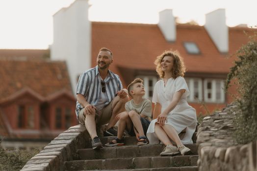 A family is talking on the stairs between roofs in an old European town. A happy father, mother, and son are having fun in the evening.