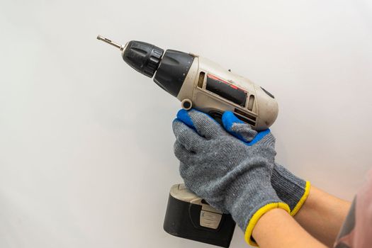 a cordless screwdriver in the hands of a man in work gloves on a white background.