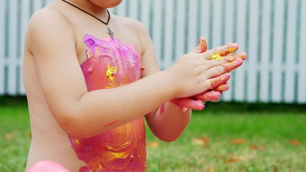 a little child, a four-year-old boy playing, painting with finger paints, decorating himself, in the garden, sitting on a blanket, on grass, lawn, in the summer. he's having fun. High quality photo