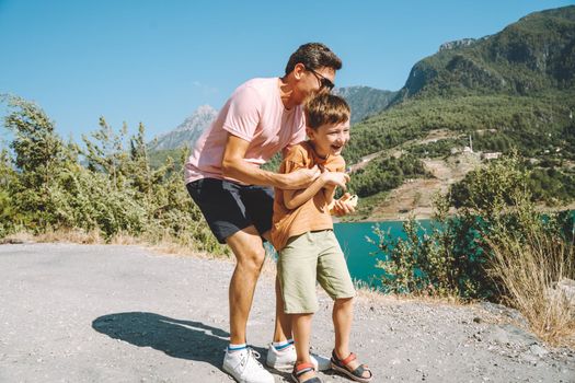 Young dad and his son standing on Mountain View. Child kid boy having fun with father and hiking hiking near mountains lake on background.