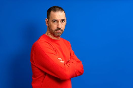 Portrait of a serious casual man standing with his hands crossed isolated on a blue background