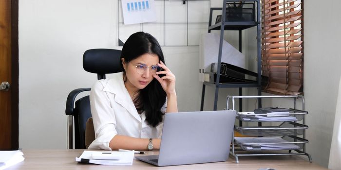 Tired female employee holding head on hand, looking at computer screen, doing hard task, having problem with computer software. Stressed exhausted businesswoman suffering from headache, feeling bored