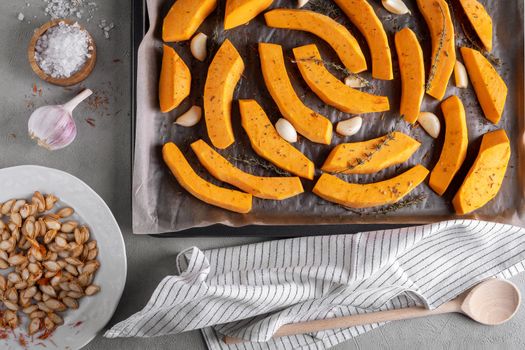 Pieces of ripe pumpkin prepared for baking in the oven. Pumpkin on a baking sheet with olive oil, garlic and dry thyme on the kitchen table. Healthy food. View from above. Selective focus.