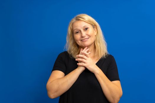 Photo portrait of a cute caucasian woman with her hands together looking impressed in admiration, dressed in a black t-shirt. Isolated on blue studio background