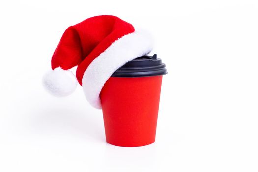Red paper cup with red Santa Claus cap on, on a white background, isolated. Close up. Copy space. Mock up