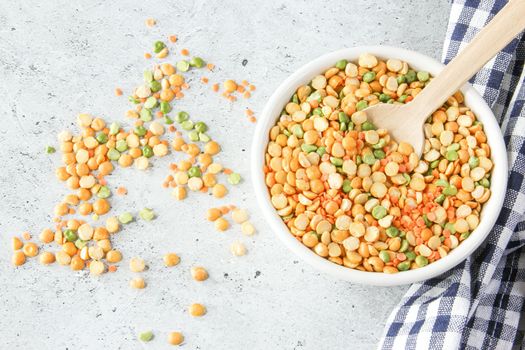 Different types of peas yellow and green in white bowl on a napkin and a light gray stone background, close up, top view.