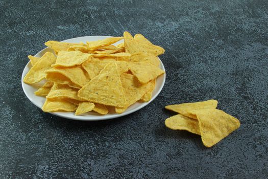 White plate with corn chips nachos on the black concrete background. Mexican chips nachos.