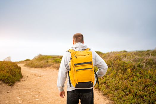 Rear-view young man with yellow backpack. Man traveler wearing grey hoodie with backpack explore nature. Wanderlust lifestyle. Mountaineering Travel Lifestyle concept.