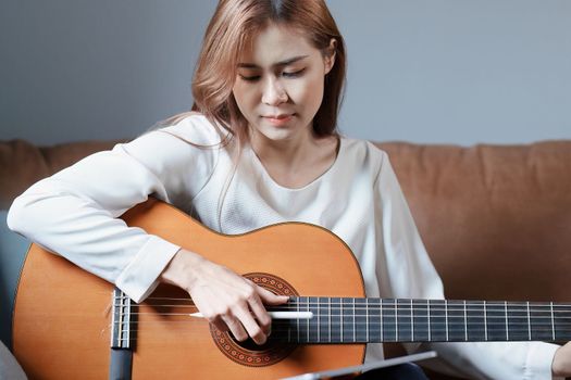 Portrait of young asian woman playing guitar on sofa relaxing stress on vacation.