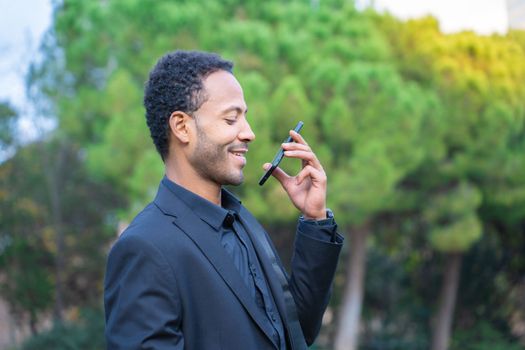 Close up portrait of attractive young black man talking on mobile phone outdoors in the city park. High quality photo