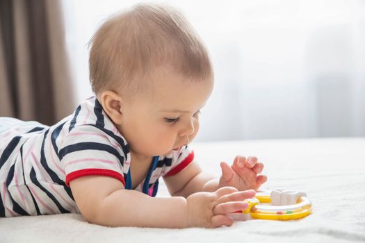 beautiful baby lies on the bed and plays by yellow toy.