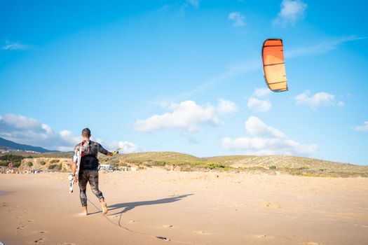 Portrait wave kitesurfer walking upwind at beach with his board and kite. Man kite surfer walk sand ocean beach with his kite surf board.