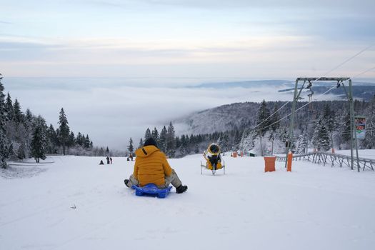 a man rides a sled against the backdrop of a magnificent winter landscape on the Wasserkuppe mountain in Ren, Hesse, Germany. magical tall and large pines and snowy firs covered with snow and ice. The horizon creates an illusion and merges with the cloudy sky and fog, which covers all the space visible in the distance. High quality photo