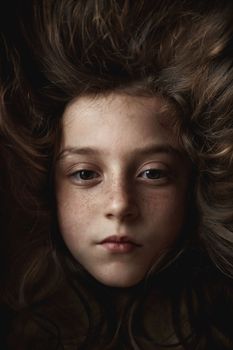 The girl's face appears on a dark hair background. Portrait of a girl shot in the studio. High quality photo