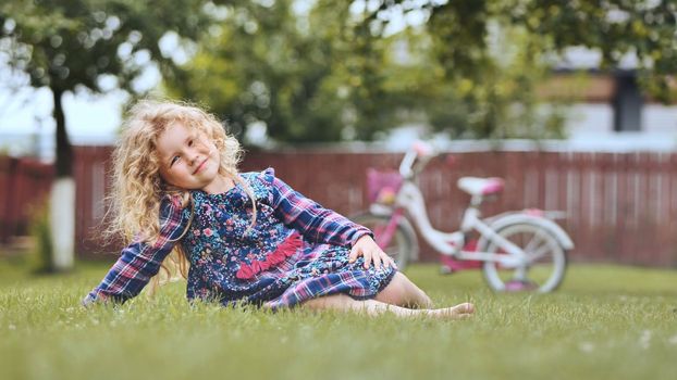 A little girl in the garden on the grass with her bicycle in the background