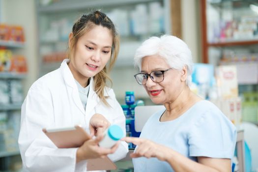 Young female pharmacist at the drugstore wearing white gown talking, giving advice, explaining, suggesting, and recommending to client or patient about the prescription and medications. Medicine and healthcare concept.