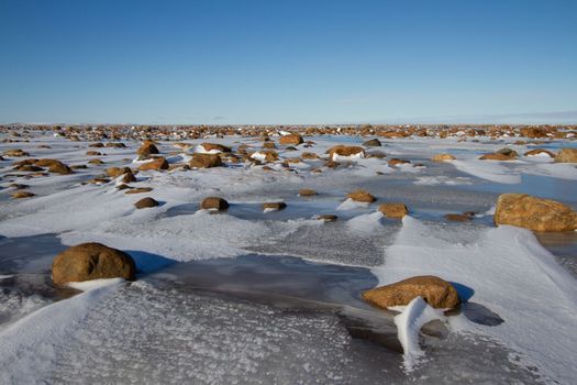 Arctic landscape - frozen arctic tundra in Nunavut over a rocky snow covered waterbody on a clear cold day, near Arviat, Nunavut